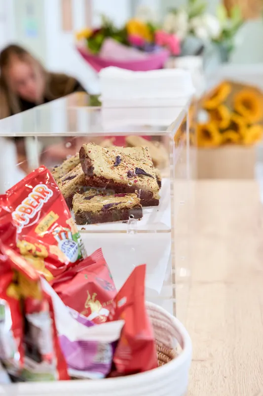 Homemade cakes and sweet treats on the counter at The Willow Bean Play Cafe, with fresh flowers behind