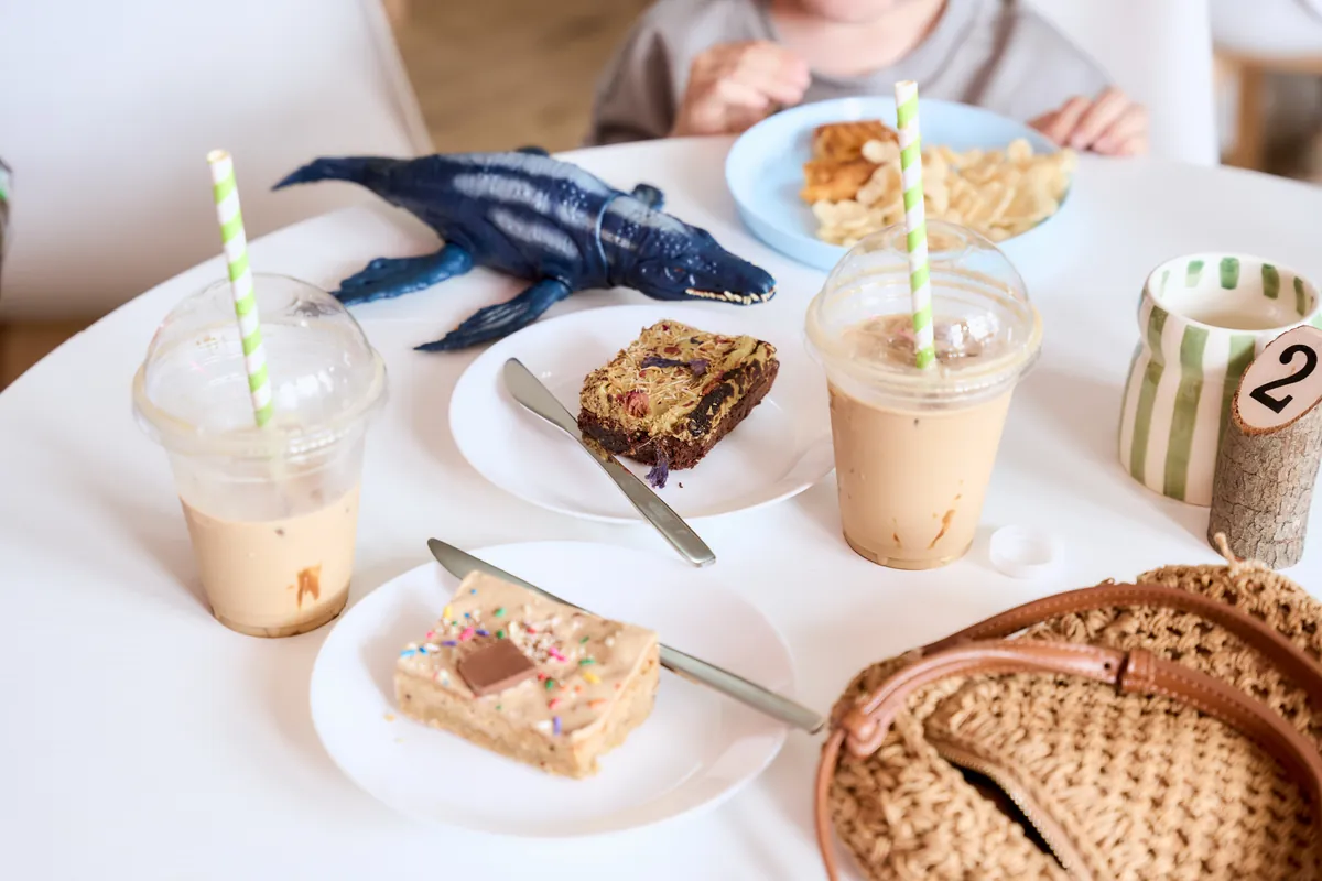 Iced lattes, homemade cake slices and a children's lunch on a cafe table at The Willow Bean