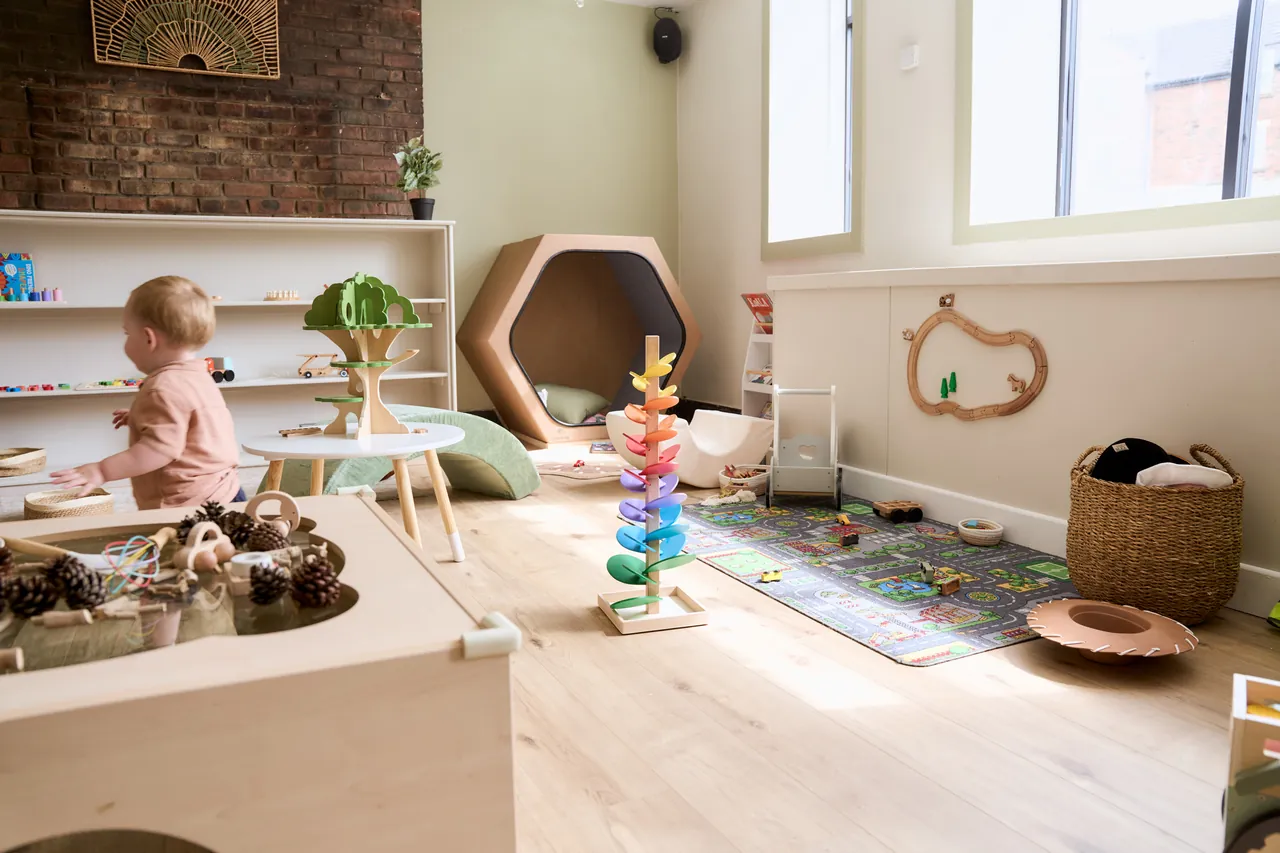 Inside The Willow Bean's play space in Bedlington — wooden toys on low open shelves, a sensory table, a cosy den and a town play rug in warm natural light