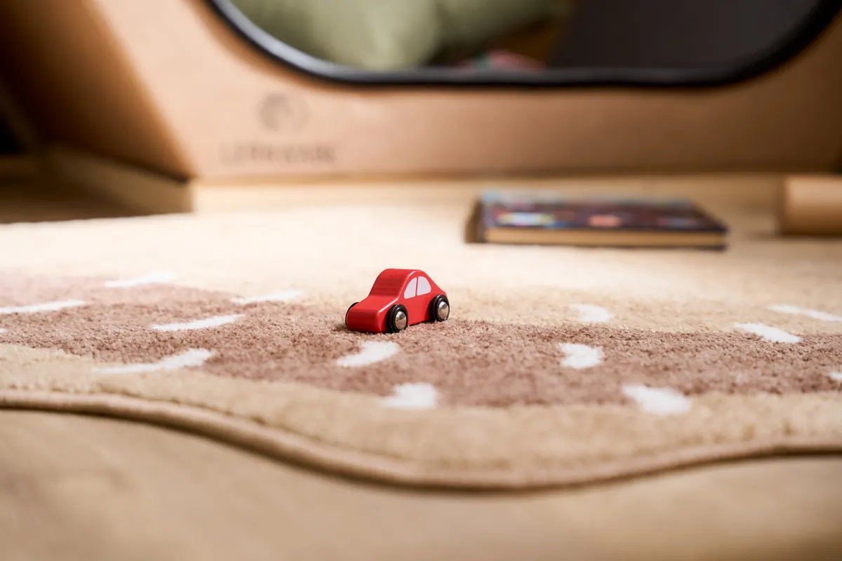 A red wooden toy car on the soft play road rug beside the cosy den